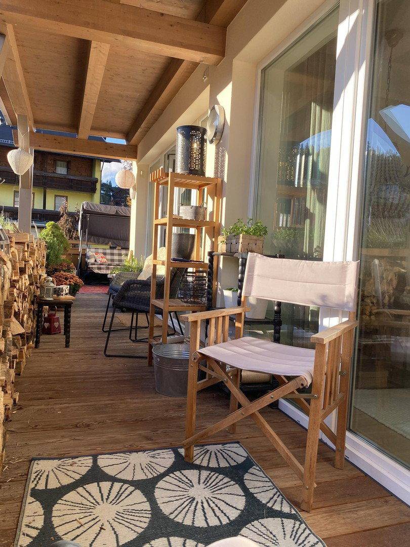 Langer überdachter Balkon mit Holzmöbeln und Blick auf die Umgebung.