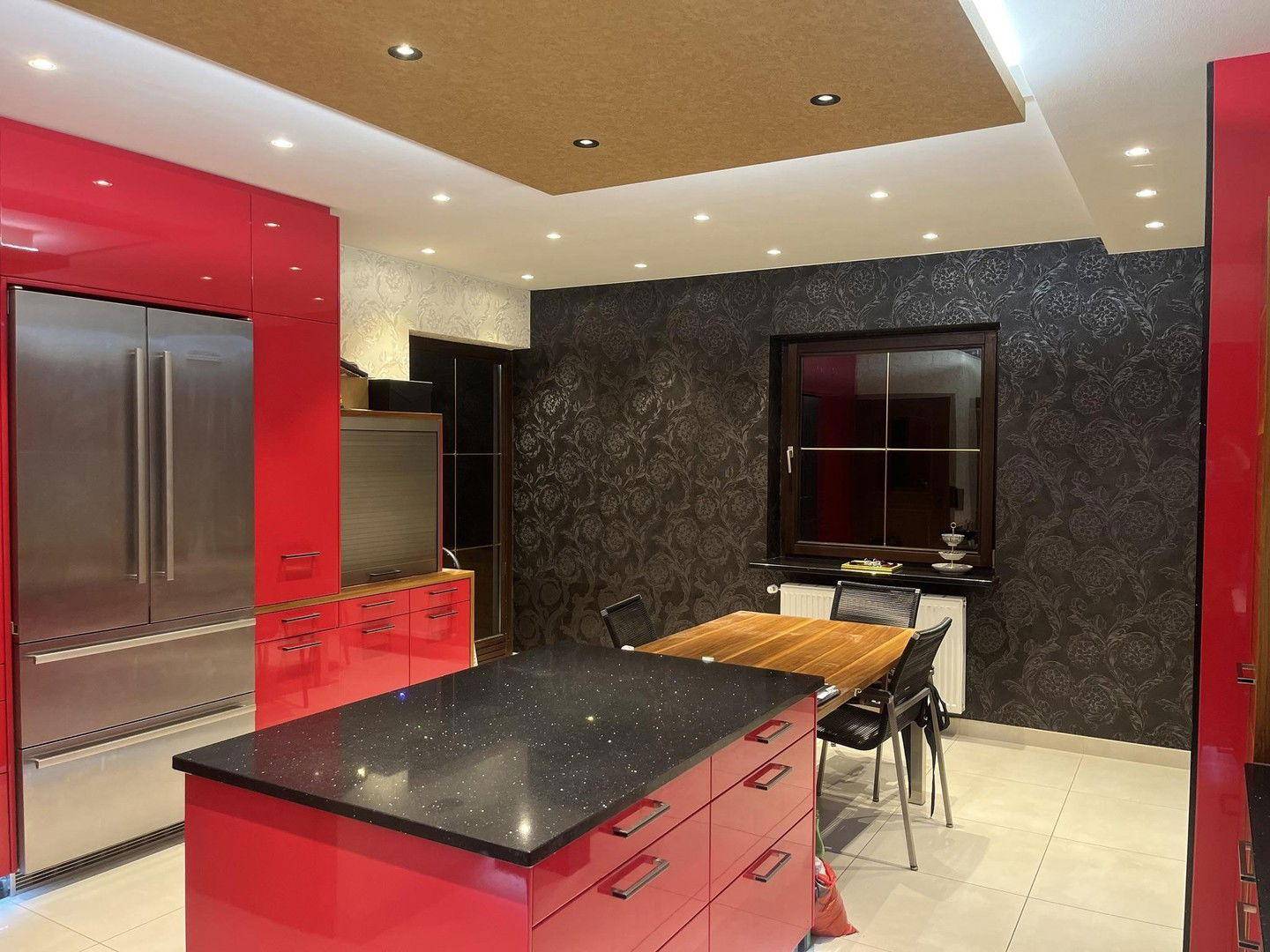 Geräumige Küche mit roter Kücheninsel, Essbereich und dunkler Tapete, gut beleuchtet.