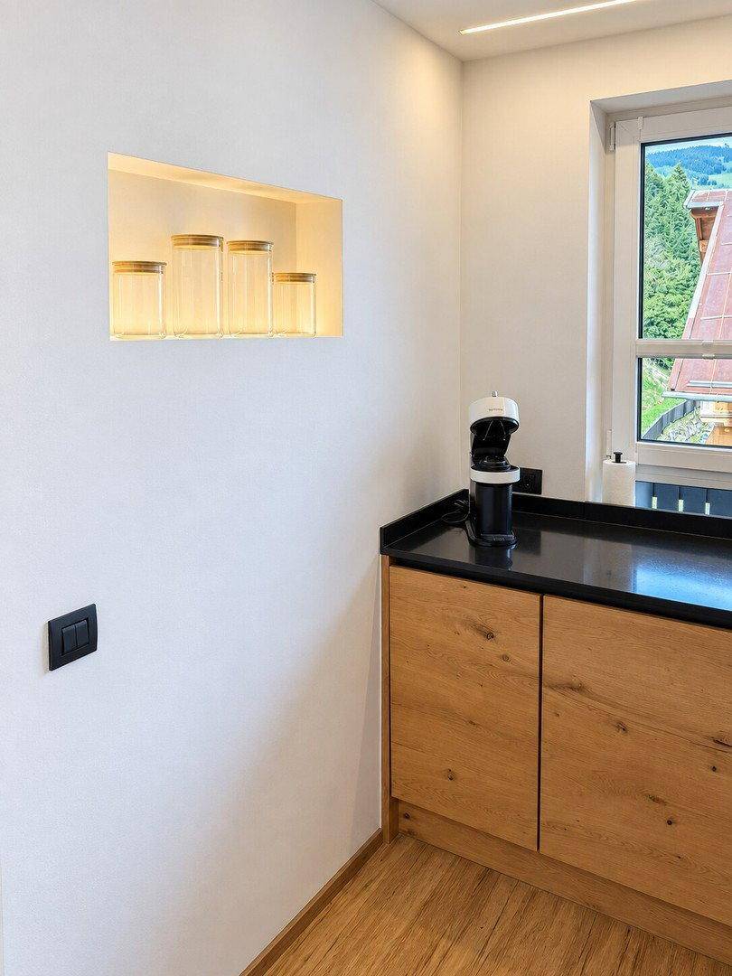 Küchenzeile mit schwarzer Arbeitsplatte, Holzelementen und Nische für Dekoration oder Vorräte.
