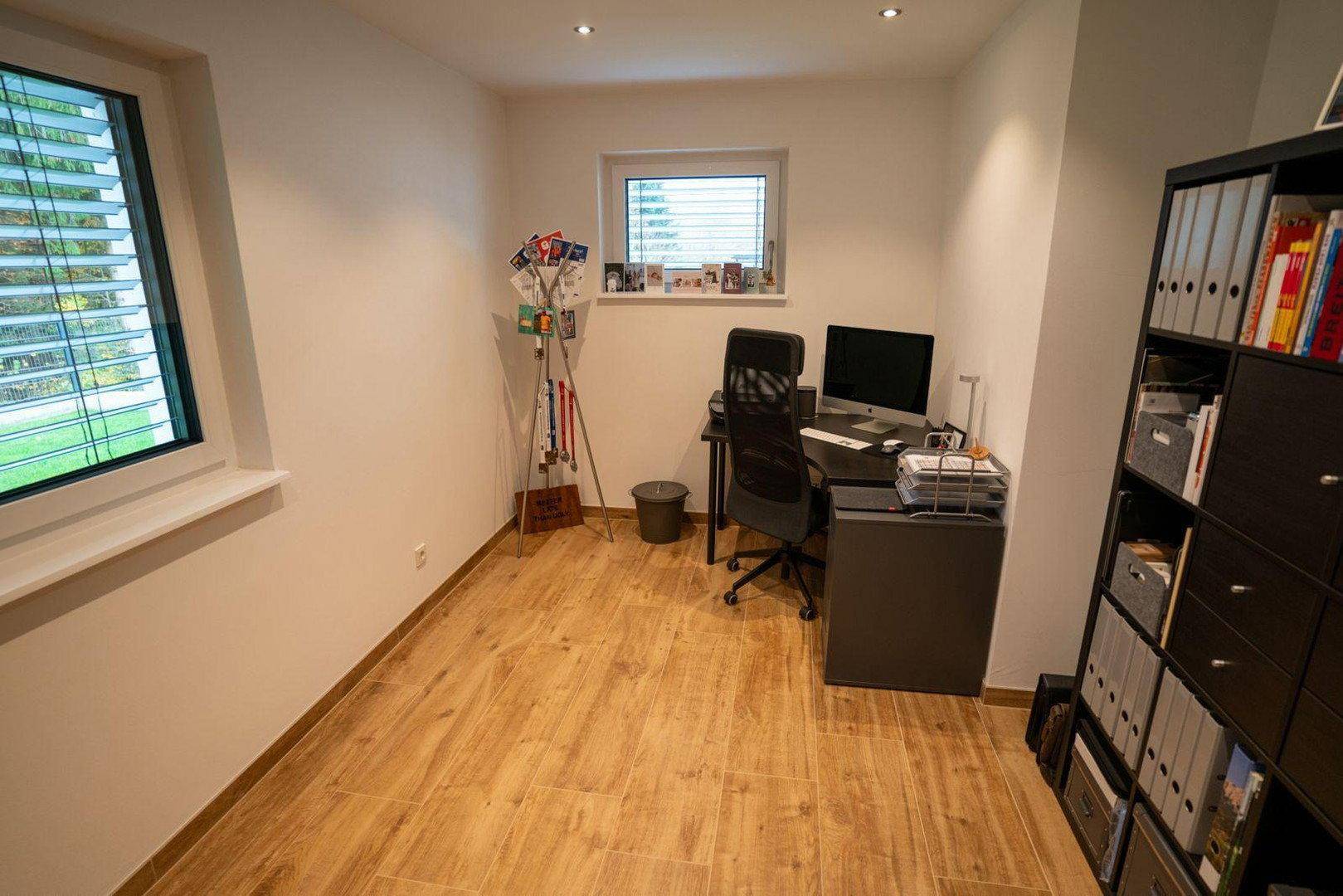 Helles Arbeitszimmer mit Schreibtisch, Bürostuhl und Regalen für Akten.