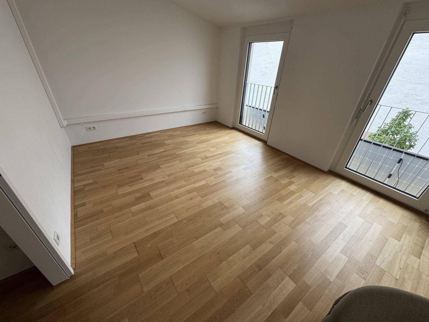 Helles Schlafzimmer mit Holzfußboden und zwei französischen Balkonen, die viel Tageslicht bieten.