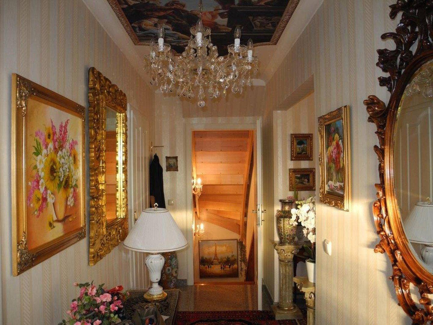 Eleganter Flur mit Kronleuchter, Spiegeln, Gemälden und Holztreppe.