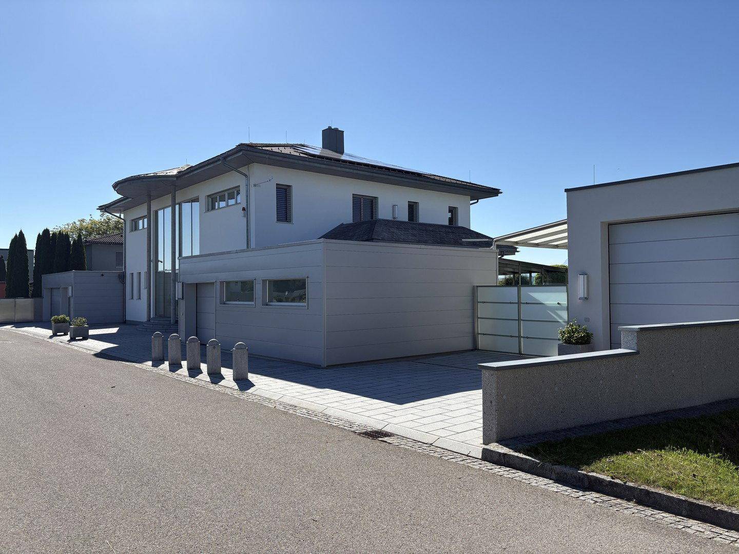 Moderne Architektur der Villa mit breiter Auffahrt, Garage und klaren Linien unter blauem Himmel.