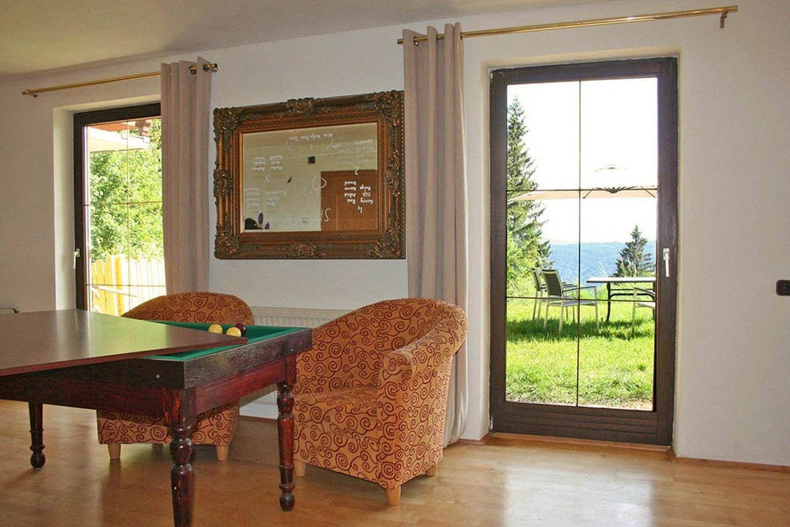 Heller Wohnbereich mit Holzboden und Fenstern, die einen Blick in den Garten ermöglichen.