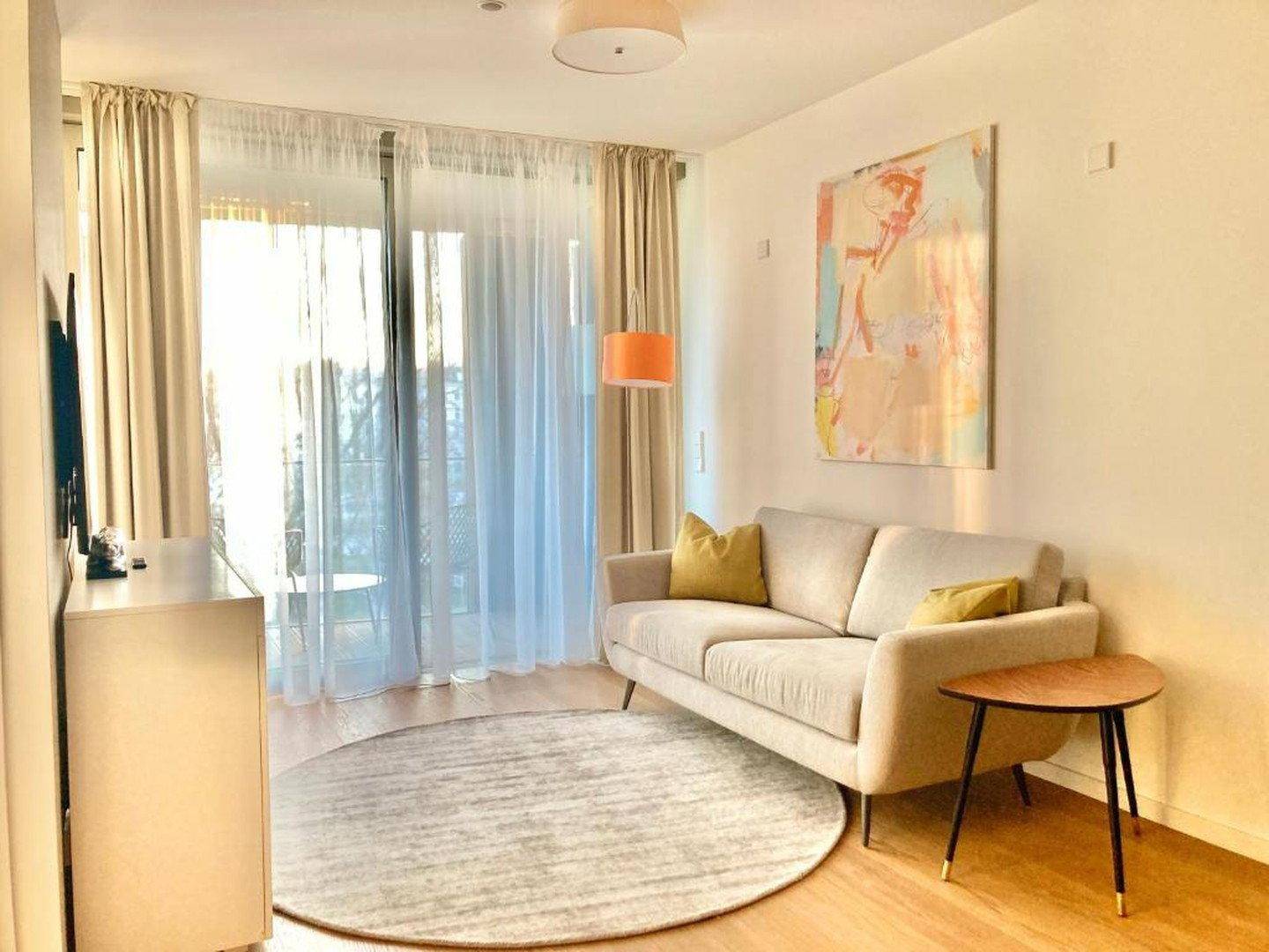 Helles Wohnzimmer mit beigem Sofa, modernem Teppich und sonnigem Balkonzugang.