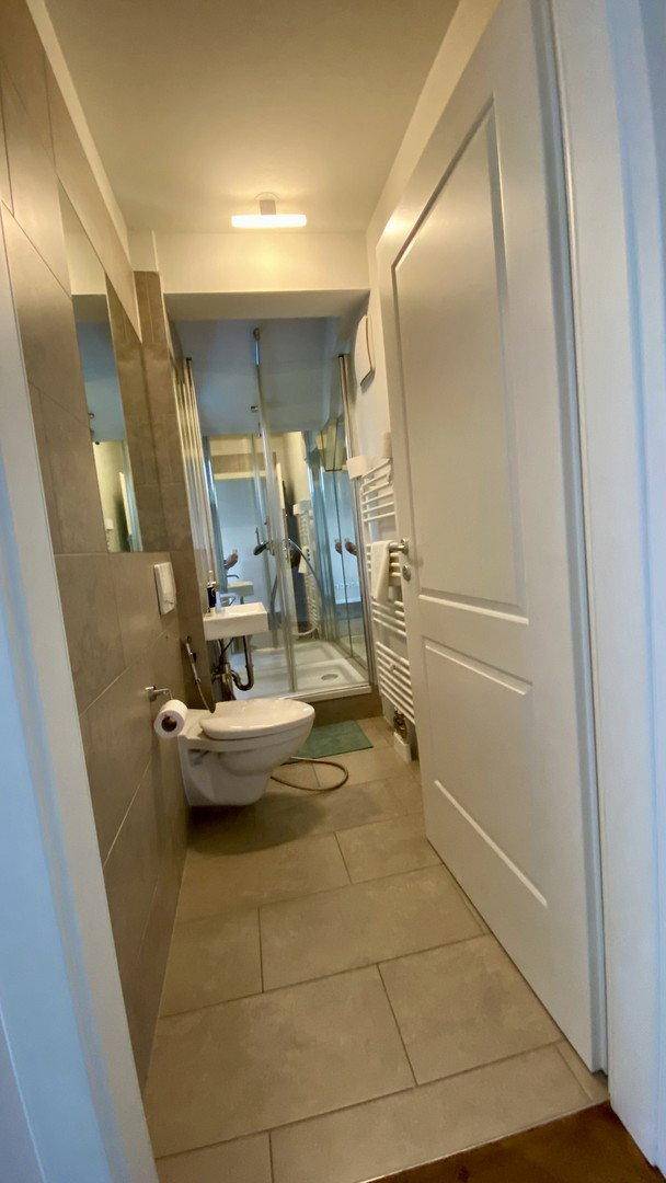 Schlichtes Badezimmer mit Dusche, wandhängendem WC und beheiztem Handtuchhalter.