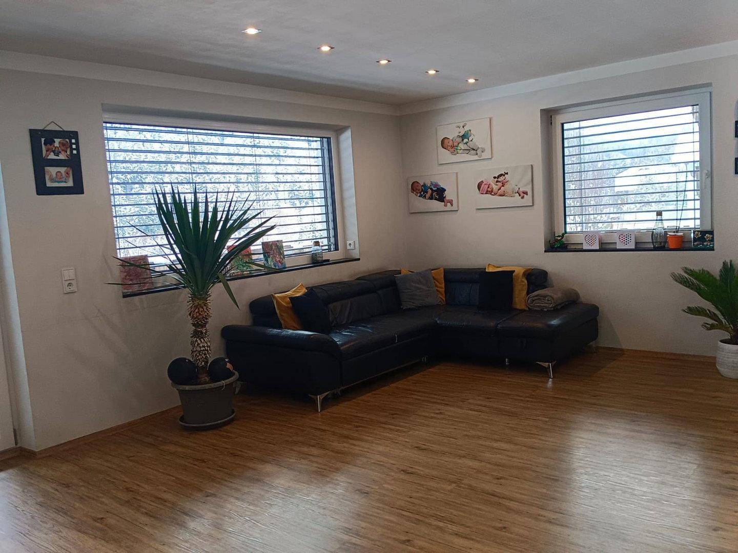 Geräumiges Wohnzimmer mit dunklem Ecksofa, Laminatboden und großen Fenstern.