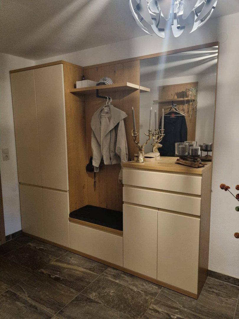 Moderner Eingangsbereich mit Garderobe, Spiegel und integrierten Schränken in hellem Holz.