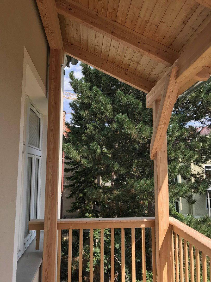 Balkon mit Holzgeländer und einem großen Nadelbaum, der für natürliche Beschattung sorgt.