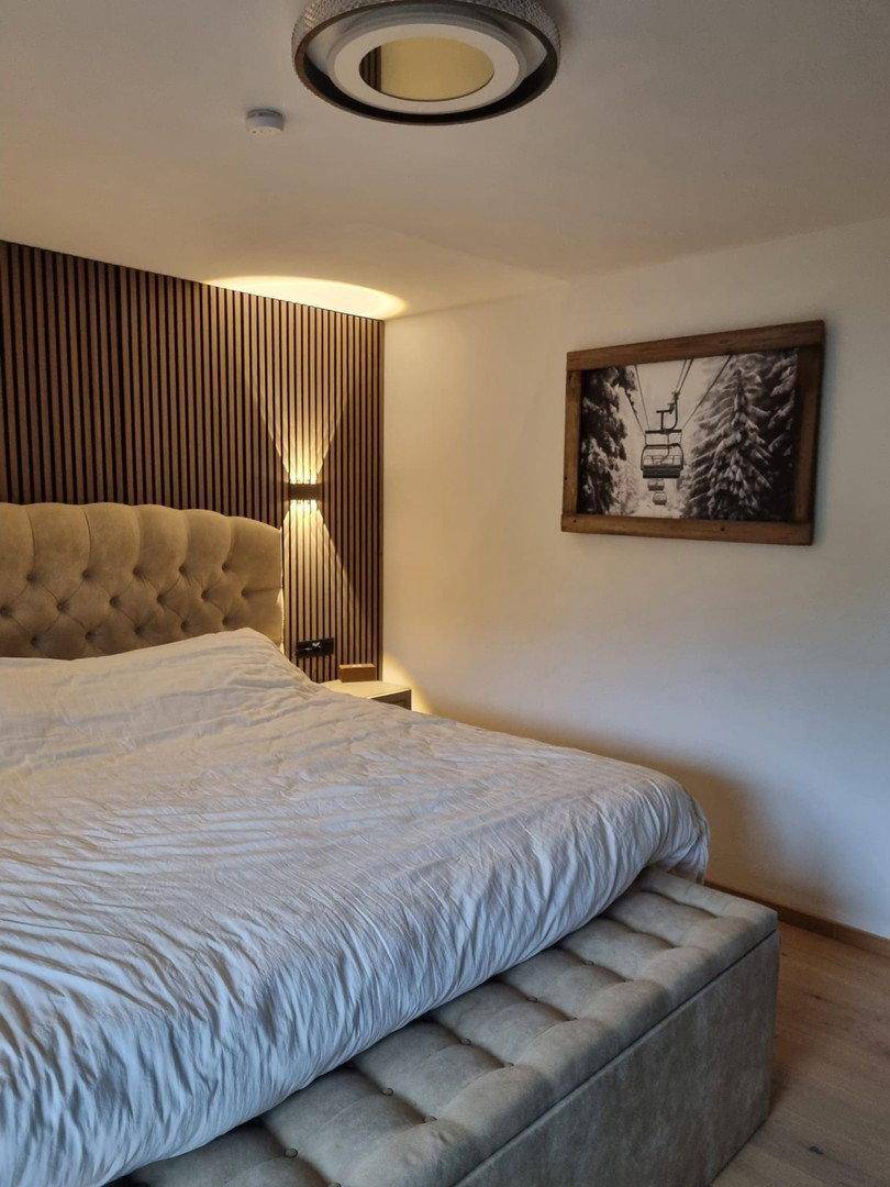 Schlafzimmer mit Polsterbett, Holzwandpaneelen und alpiner Kunst an der Wand.