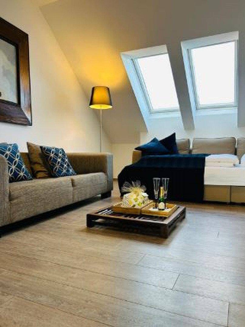 Heller Wohnbereich mit Holzboden, beiger Couch, Dachfenstern und einem Tablett mit Sektgläsern.
