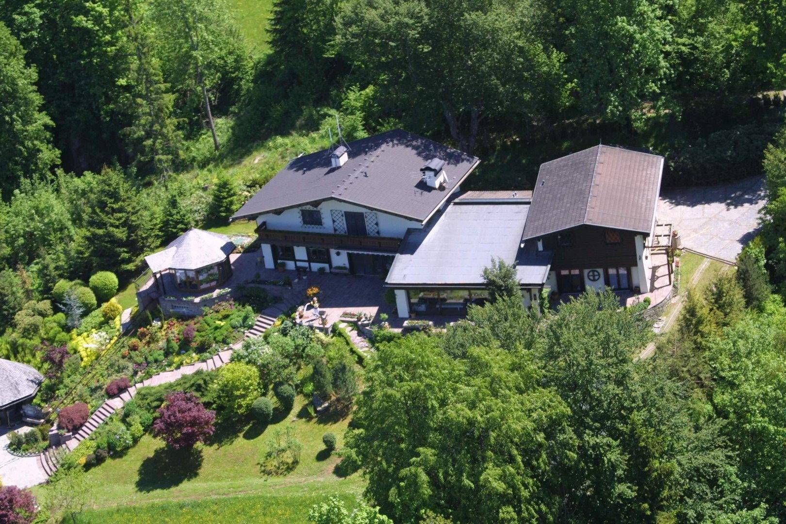 Vogelperspektive eines großen Hauses mit mehreren Gebäudeteilen und einem gepflegten Gartenbereich.