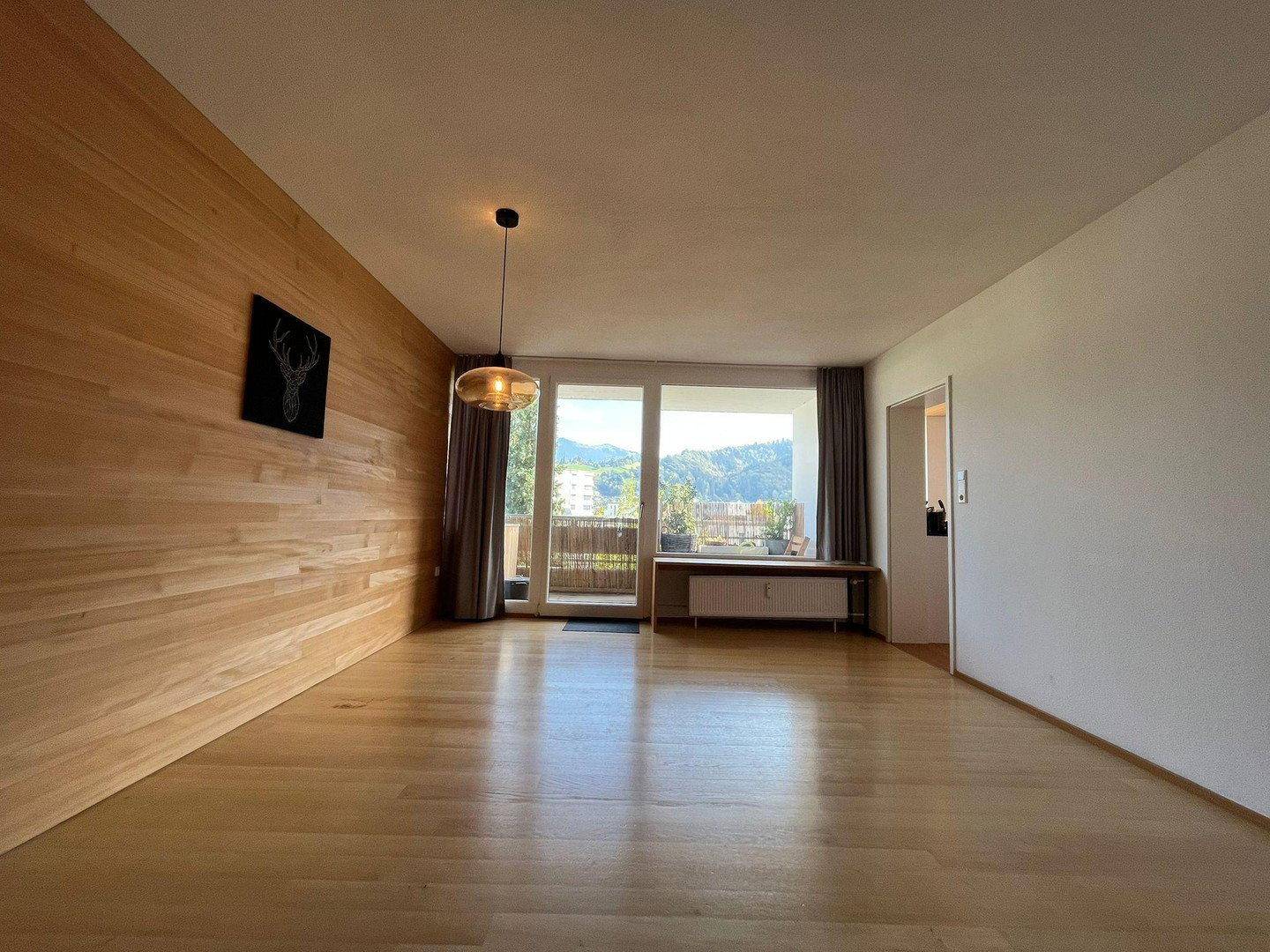 Helles Wohnzimmer mit Holzboden, einer Holzwand und Zugang zu einem Balkon mit Bergblick.