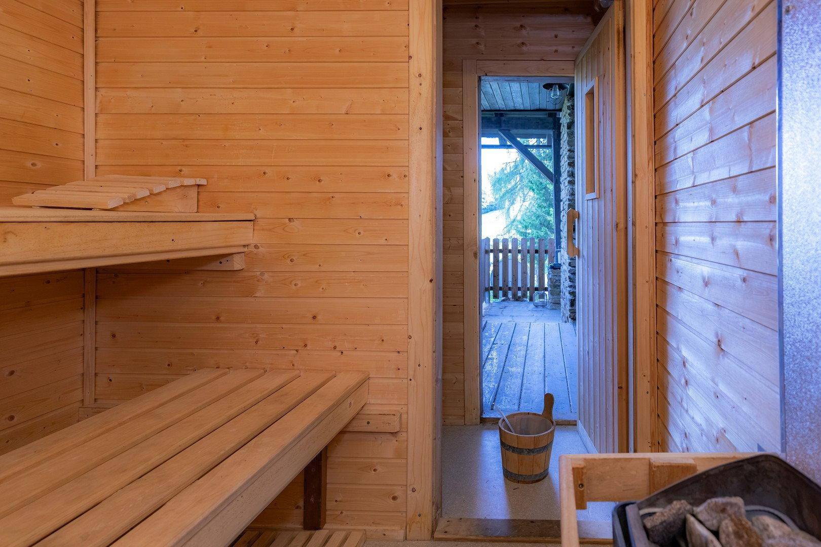 Traditionelle Holzsauna mit Bänken und Saunaofen, mit Zugang zu einem Außenbereich.