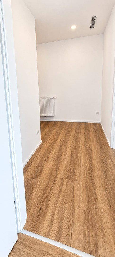 Schmaler Flur mit Laminatboden und weißen Wänden, der einen Übergang zu einem weiteren Raum bildet.