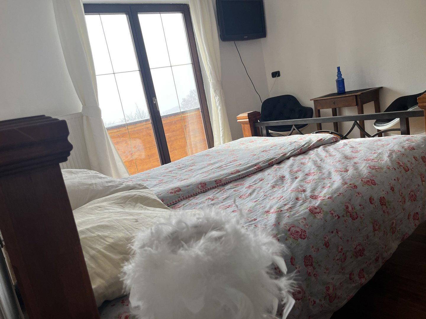 Nahaufnahme eines Bettes mit floraler Bettwäsche und einem hellen Fenster, das den Himmel zeigt.