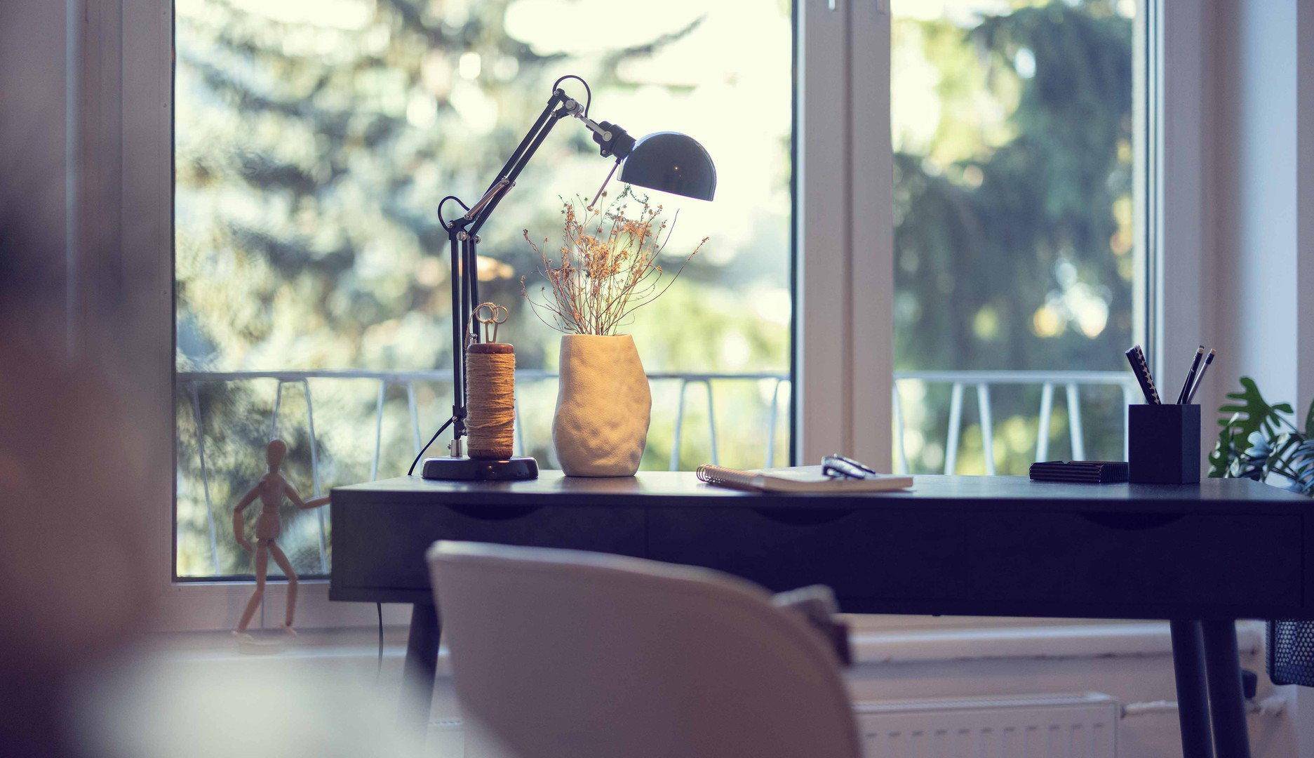Detailaufnahme des Schreibtischs am Fenster mit Blick auf Bäume und viel Tageslicht.