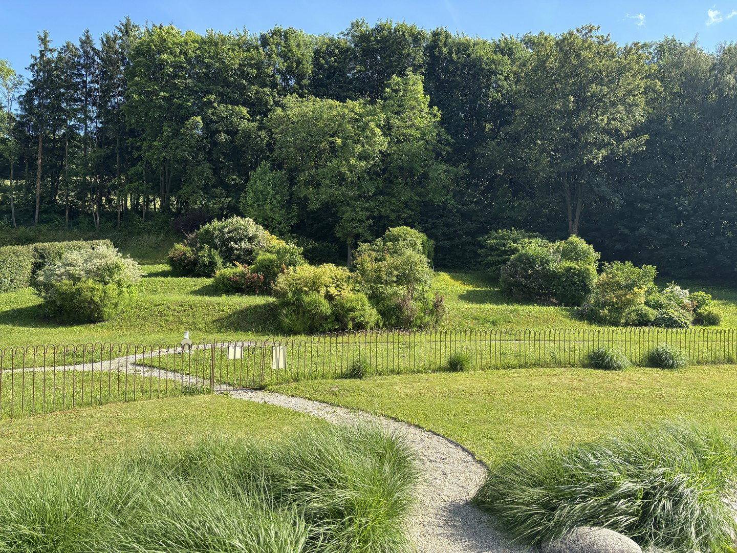 Gepflegter Gartenbereich mit Rasenflächen, Sträuchern und einem geschwungenen Kiesweg.