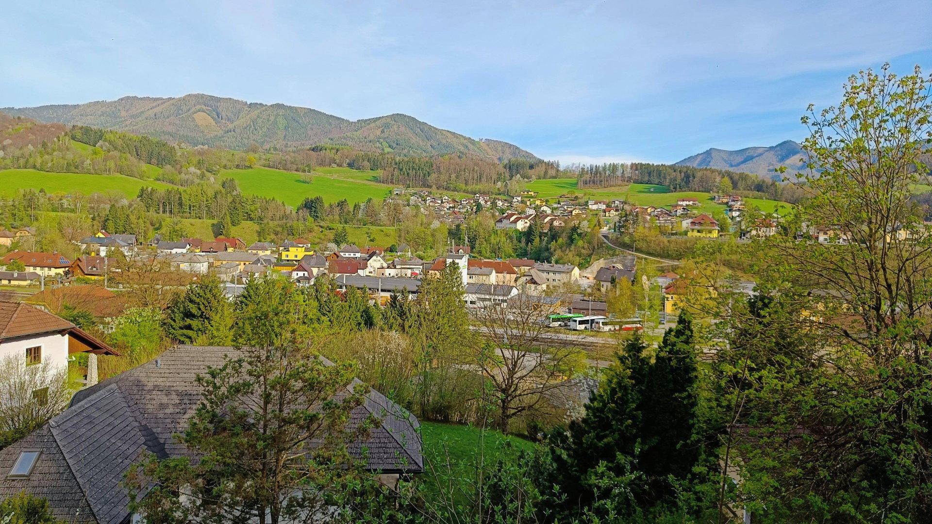 Malerischer Panoramablick auf eine charmante Stadt in einem Tal, umgeben von grünen Bergen.