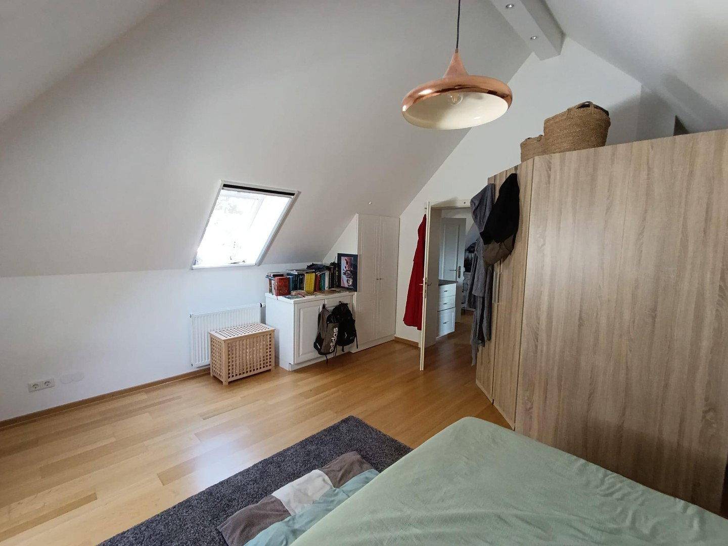Gemütliches Schlafzimmer im Dachgeschoss mit Holzboden, Dachfenster und Kleiderschrank.