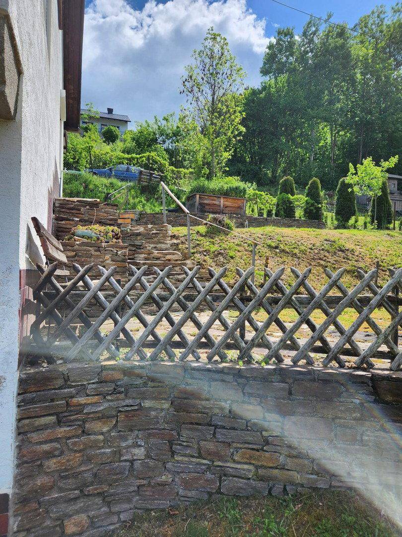 Steinmauer und Holzzaun mit terrassiertem Gartenbereich und Stufen, die einen Hang hinaufführen.