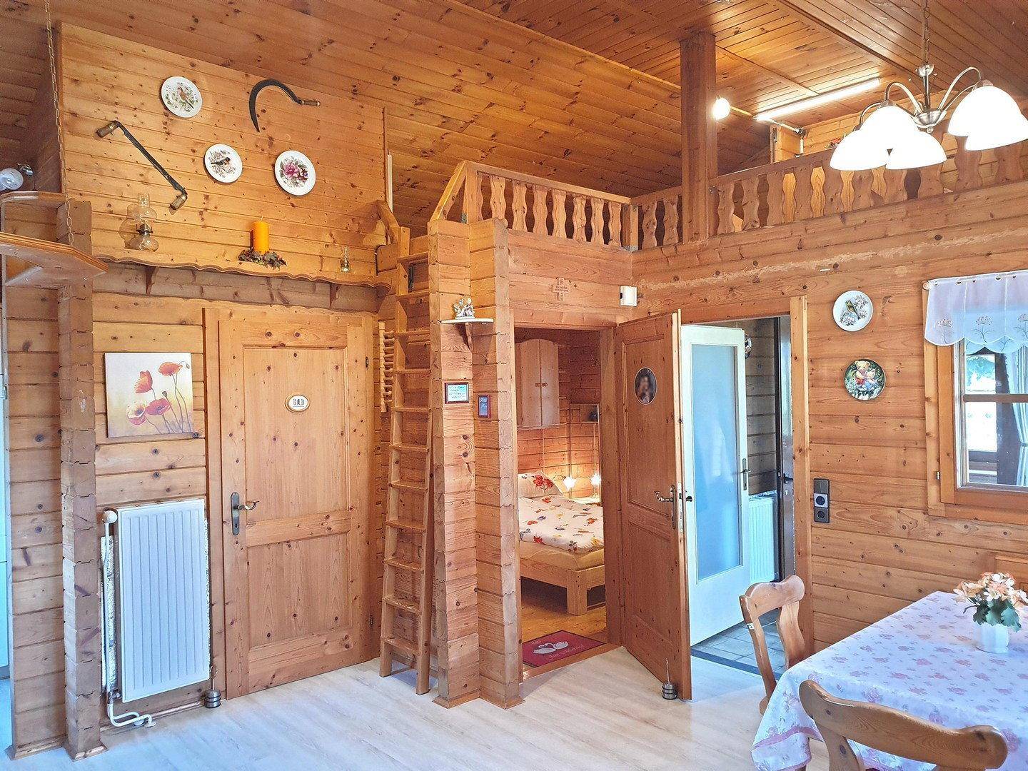 Offener Wohnbereich mit Holzwänden, Essbereich und Zugang zu einem gemütlichen Schlafzimmer.