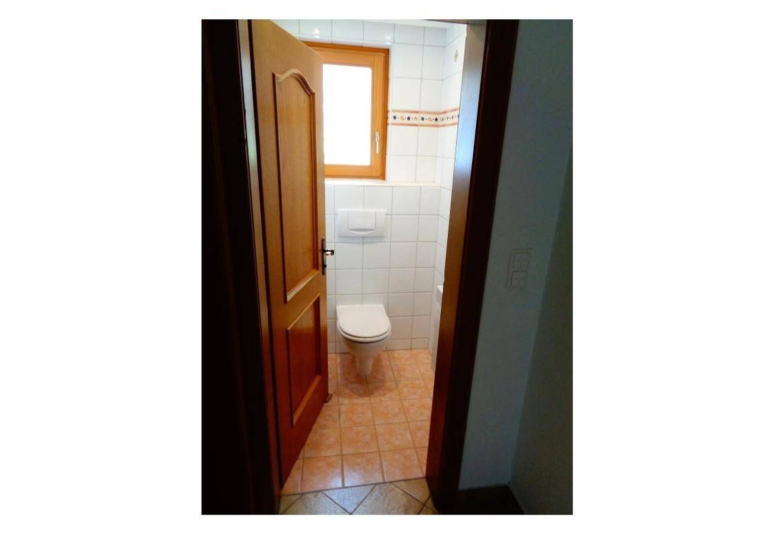 Kleines WC mit weißen Wandfliesen, Fenster und Terrakotta-Bodenfliesen, funktional und hell.