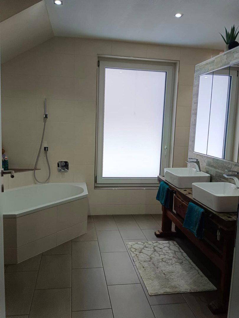 Helles Badezimmer mit Eckbadewanne, Doppelwaschbecken und großem Fenster.