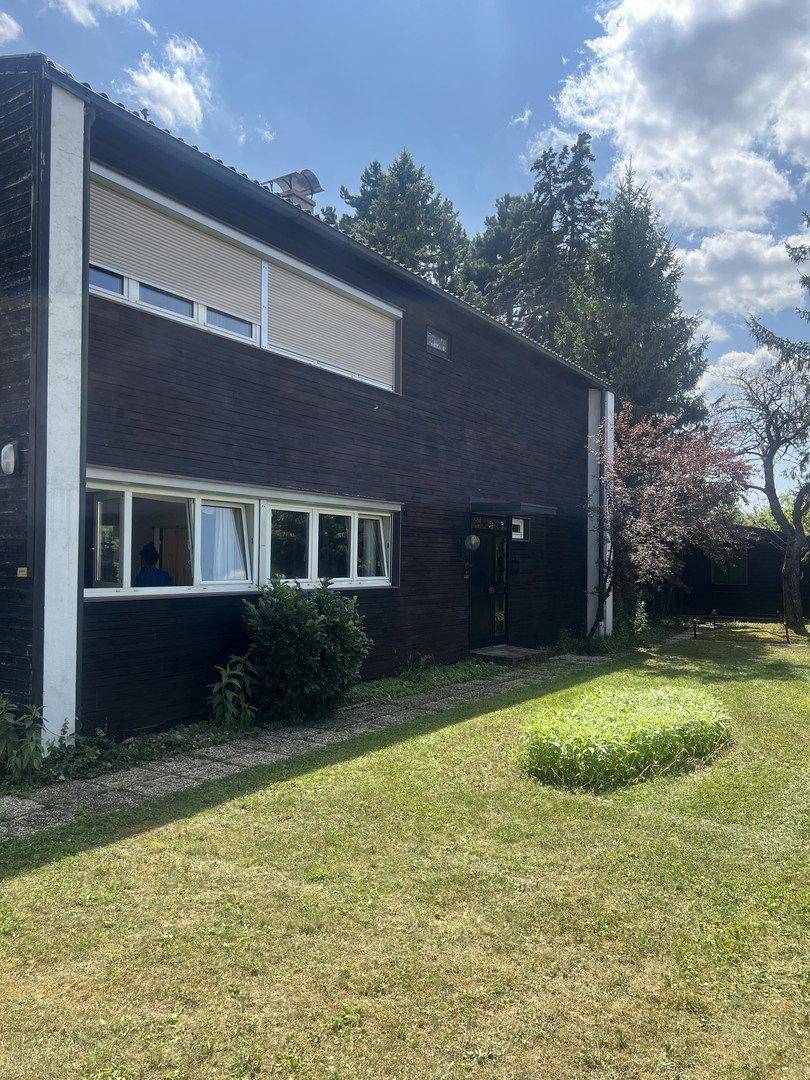 Seitenansicht des Hauses mit dunkler Fassade, Fenstern und Rollläden sowie einem gepflegten Garten.