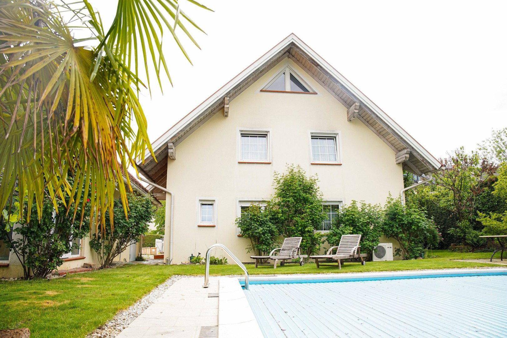 Rückseite des Hauses mit einem großen Pool und zwei Liegestühlen auf der Rasenfläche im Garten.