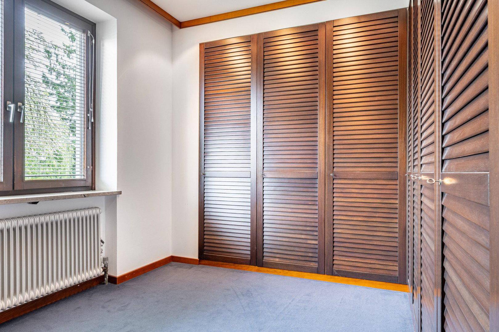 Schlafzimmer mit Einbauschränken aus Holz und Teppichboden, hell beleuchtet.