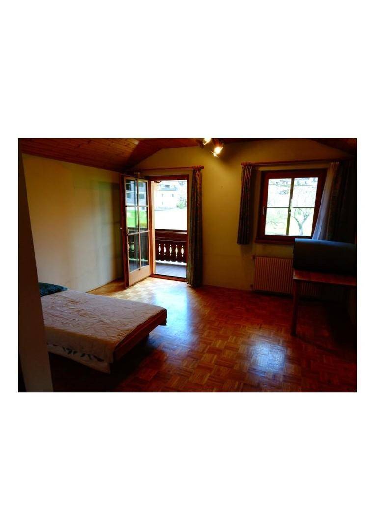 Schlafzimmer mit Holzboden, Balkonzugang und Blick auf die grüne Umgebung, ausgestattet mit einem Bett.