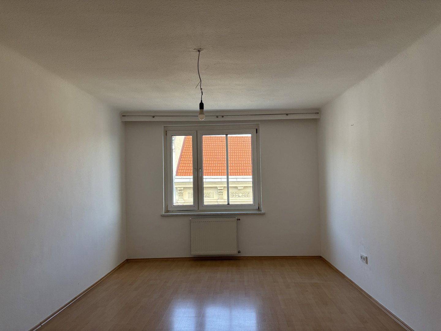 Geräumiges, helles Zimmer mit Holzfußboden und einem Fenster mit Blick auf die umliegenden Gebäude.