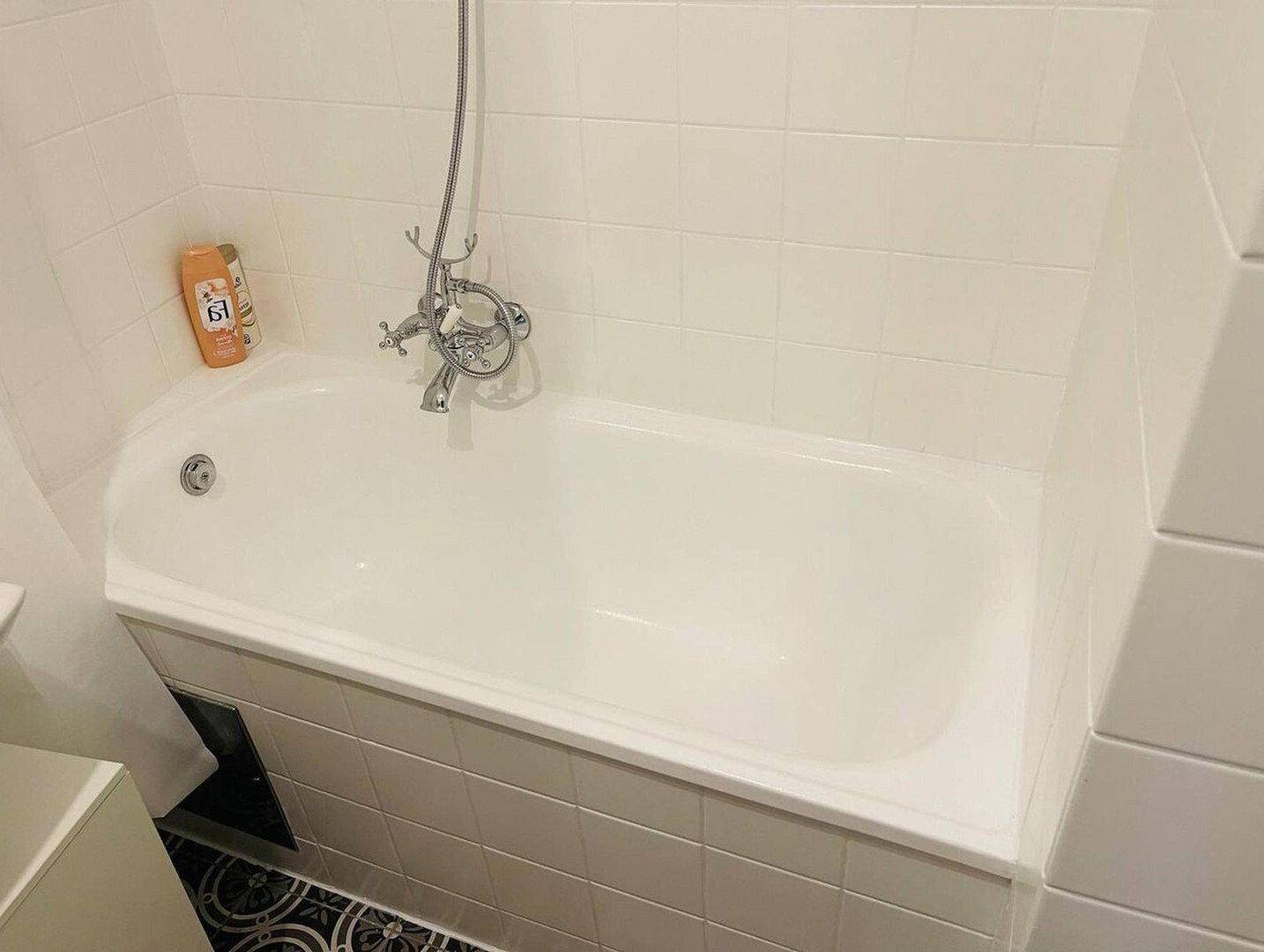 Eingebaute Badewanne mit weißen Fliesen und Duscharmatur in einem hellen Badezimmer.