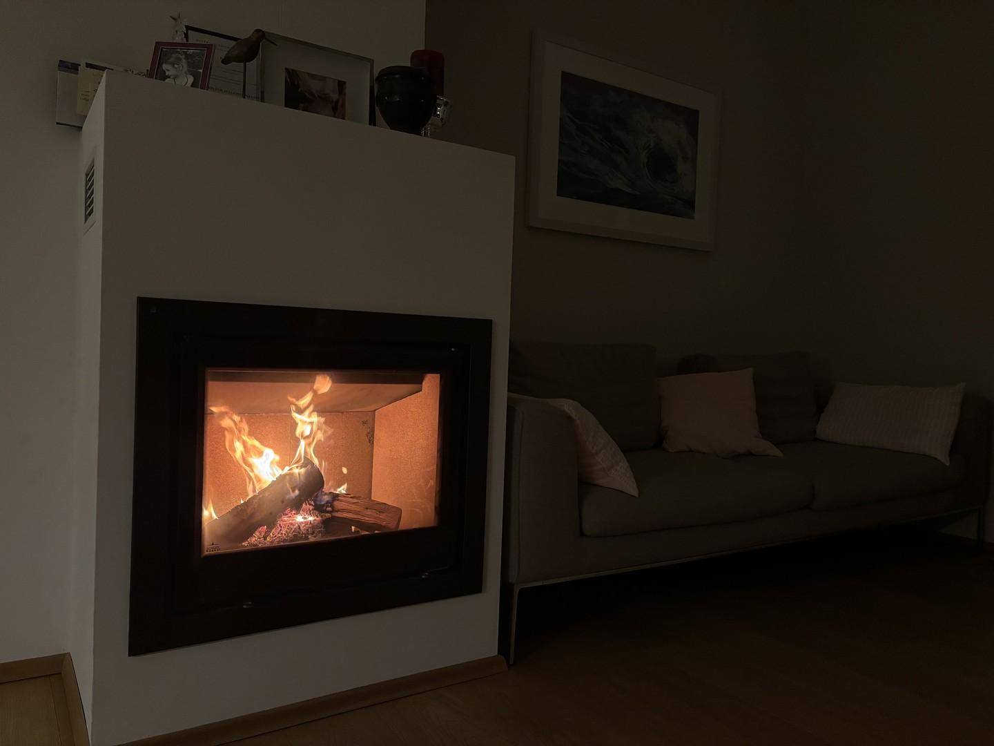 Gemütliches Wohnzimmer am Abend mit brennendem Kamin und gedämpfter Beleuchtung.