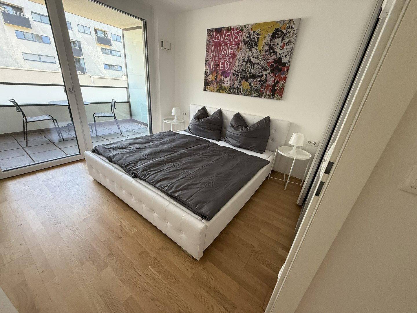 Schlafzimmer mit Balkonzugang, Doppelbett und Blick auf den möblierten Außenbereich.