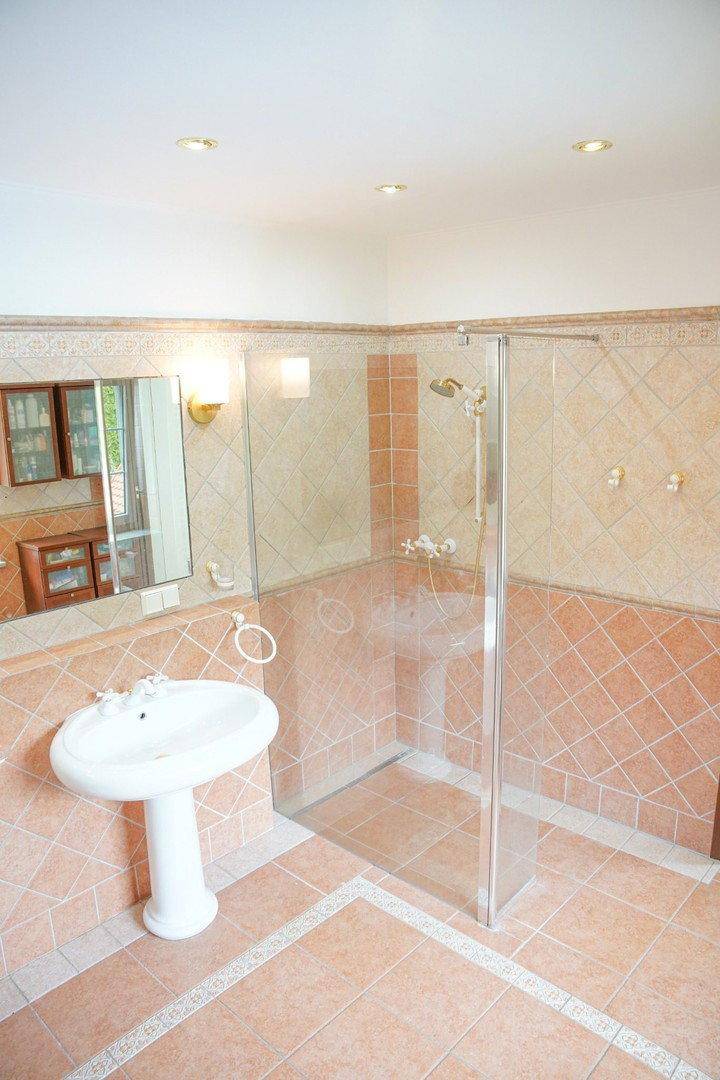 Duschbereich mit Glaswand und Waschbecken in einem gefliesten Badezimmer.