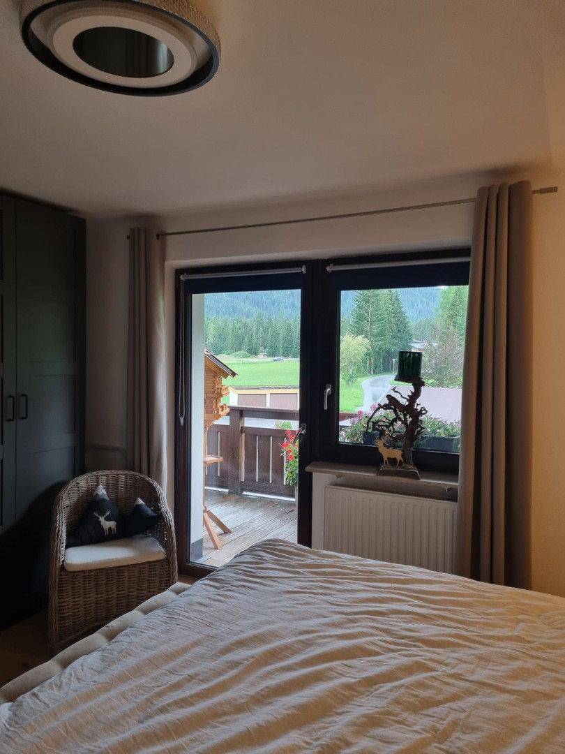 Schlafzimmer mit Balkonzugang, Holzboden und Blick auf die grüne Landschaft und Berge.