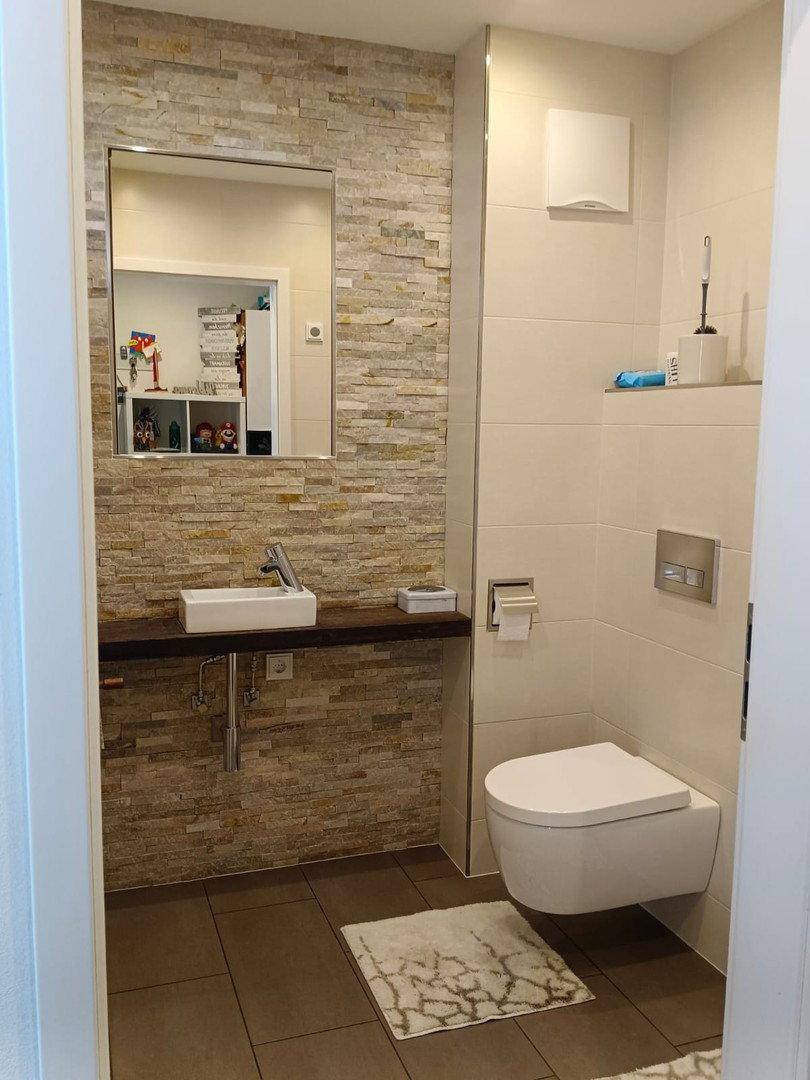 Modernes Badezimmer mit wandhängender Toilette, Aufsatzwaschbecken und Spiegel.