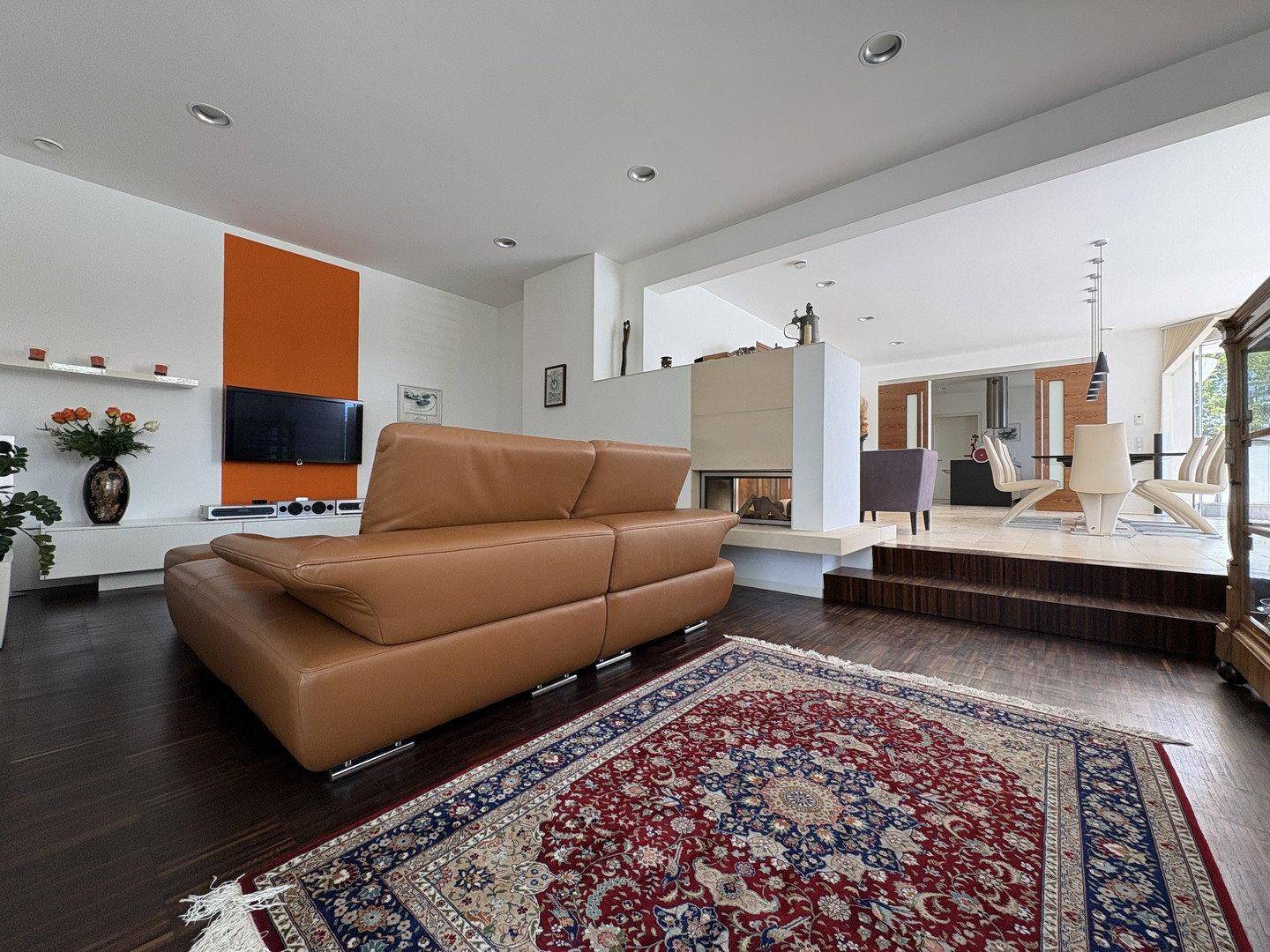 Gemütlicher Wohnbereich mit Ledersofa, modernem Kamin und angrenzendem Essbereich auf erhöhter Ebene.