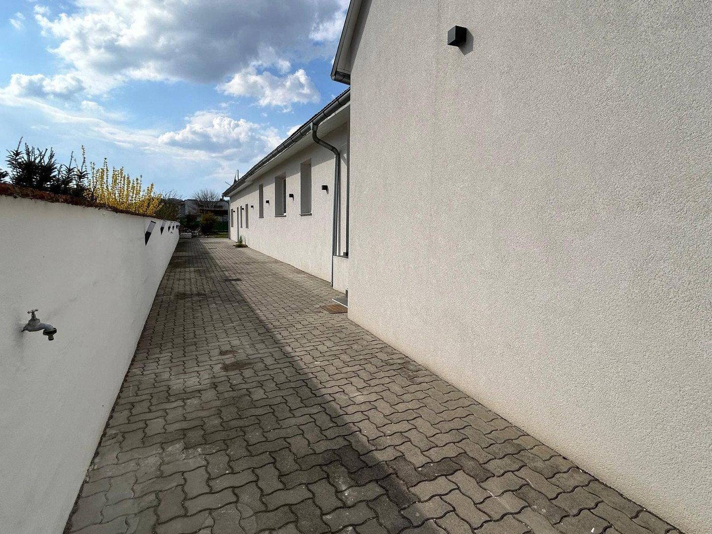 Seitenansicht eines weißen Gebäudes mit gepflastertem Weg unter blauem Himmel.