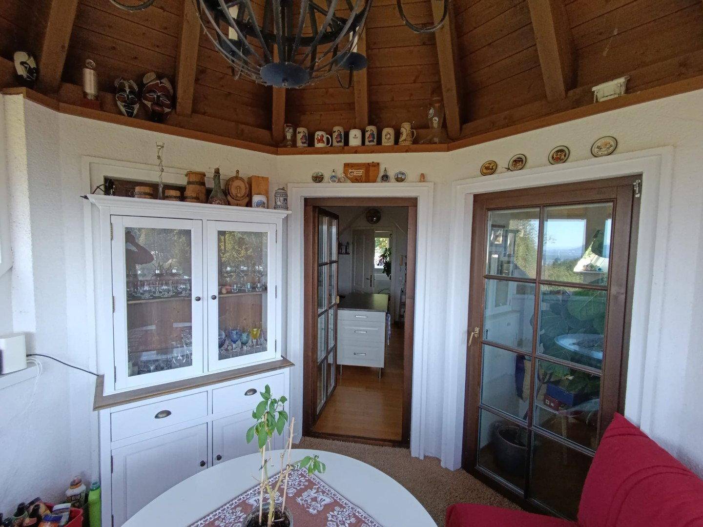 Heller Wintergarten mit Holzbalkendecke, Vitrine und Zugang zu weiteren Räumen.