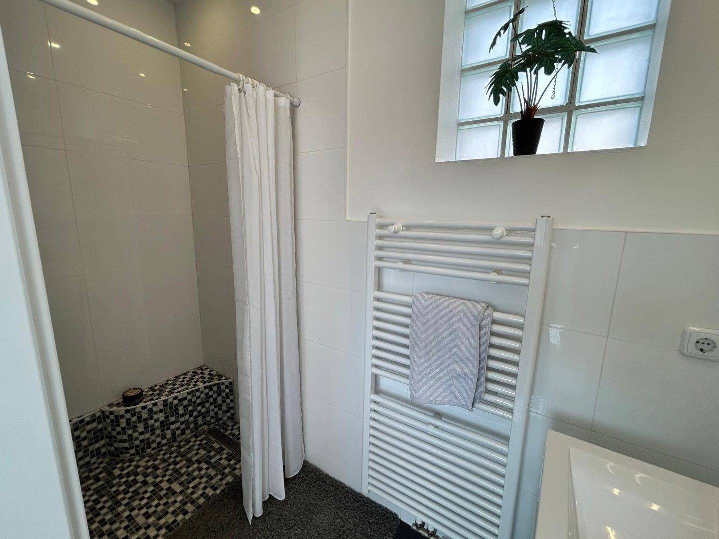 Geräumige Dusche mit Fliesenbank, Duschvorhang und beheiztem Handtuchhalter im Badezimmer.
