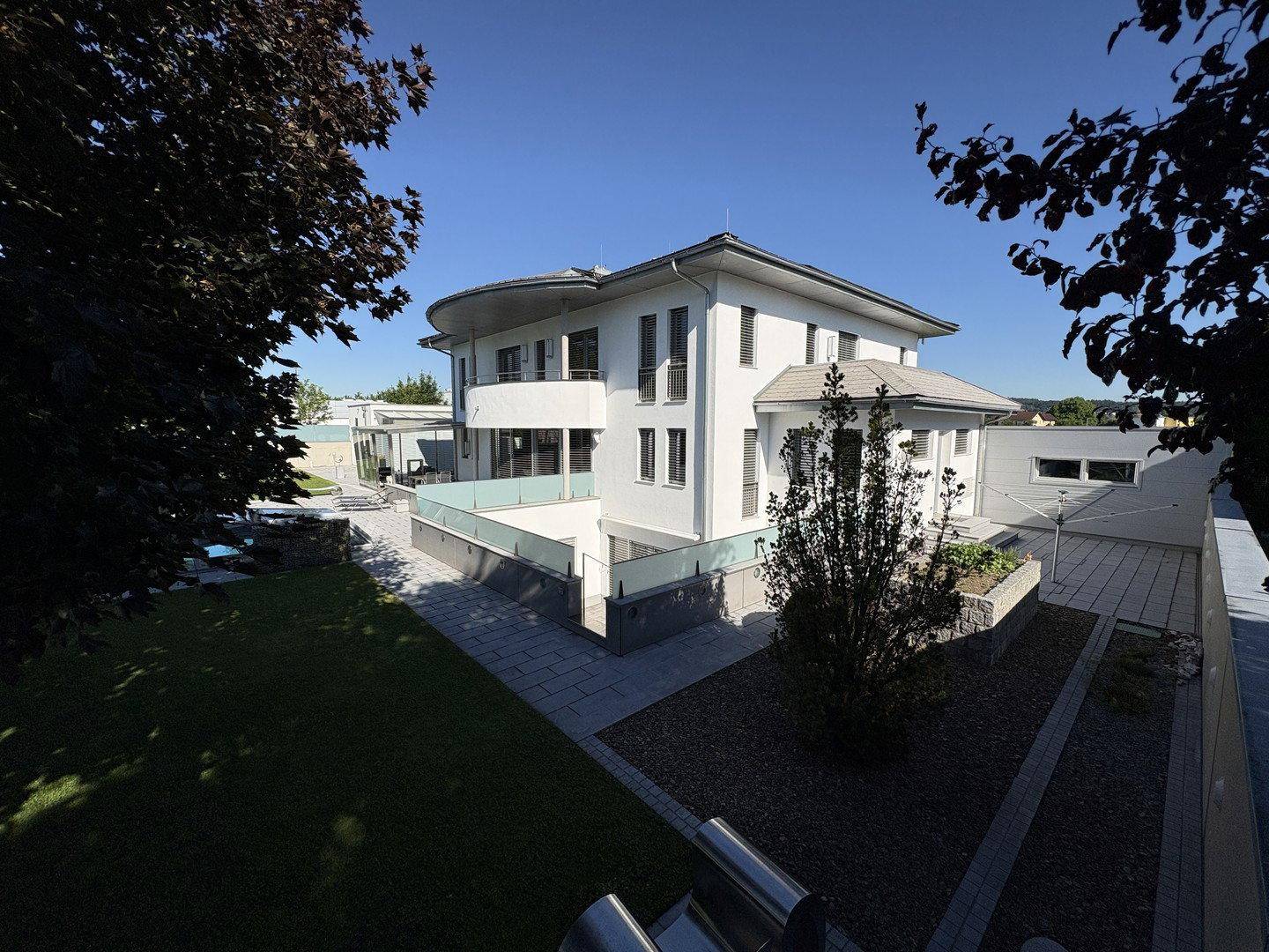 Elegante moderne Villa mit weißer Fassade und gepflegter Außenanlage unter strahlend blauem Himmel.