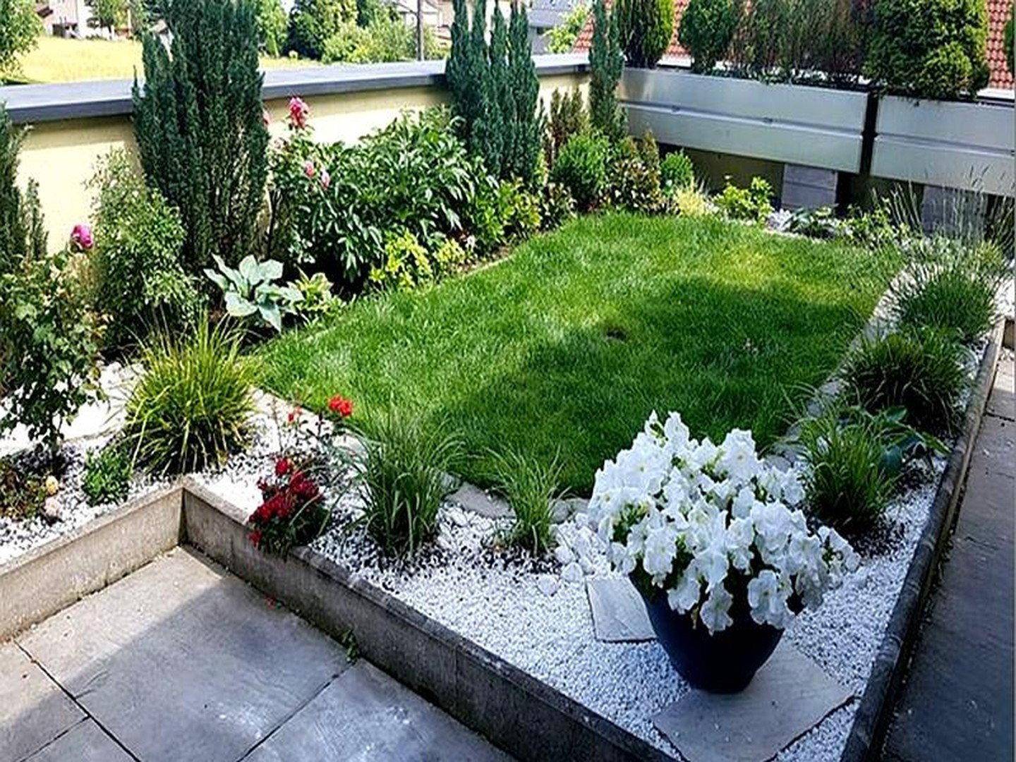 Kleiner, gepflegter Garten mit Rasenfläche, Blumenbeeten und Ziersträuchern.