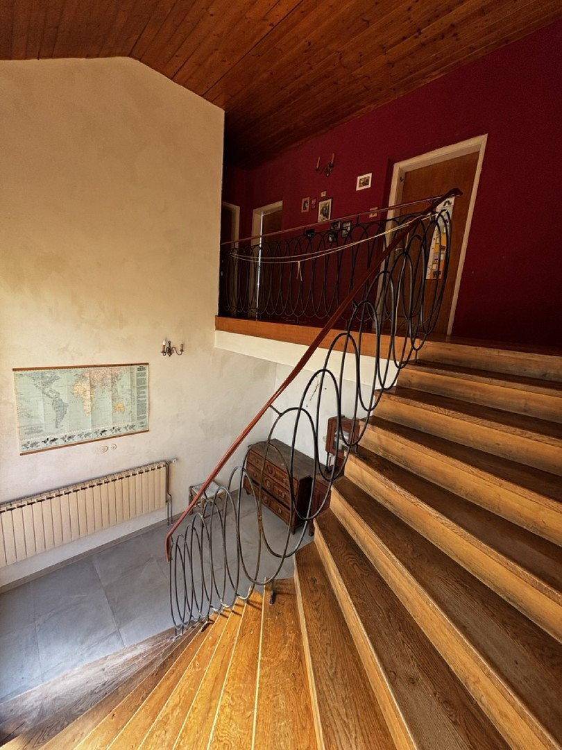 Treppenhaus mit Holzstufen, schmiedeeisernem Geländer und roter Akzentwand.