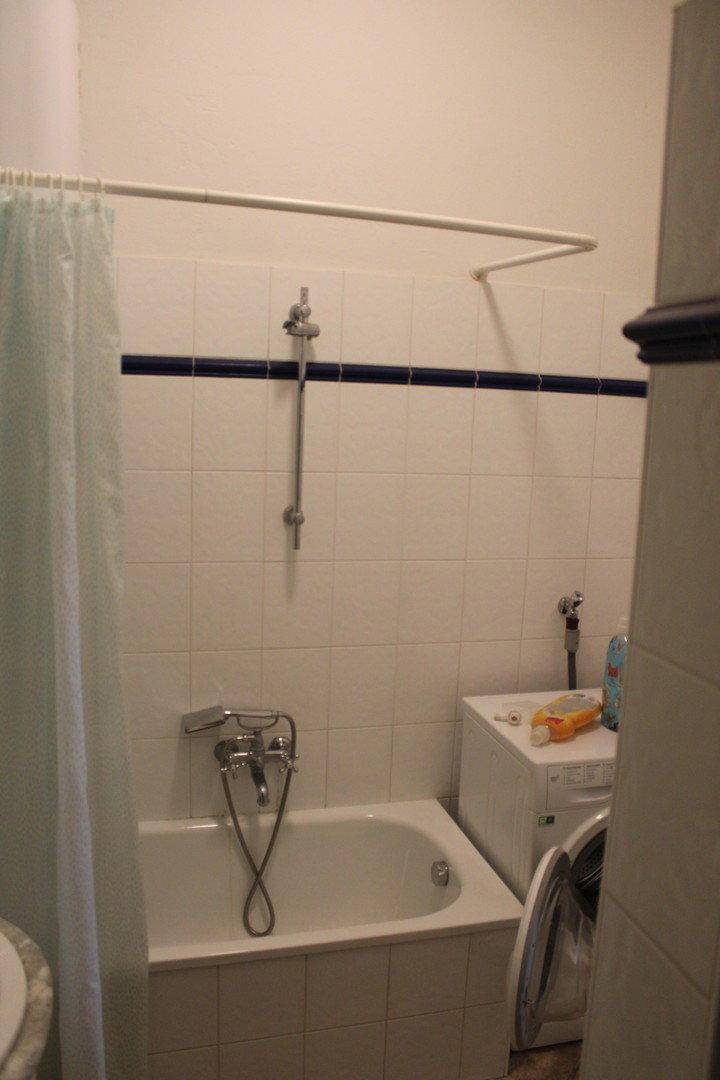 Badezimmer mit Badewanne, Duschvorrichtung und einer Waschmaschine im Hintergrund.