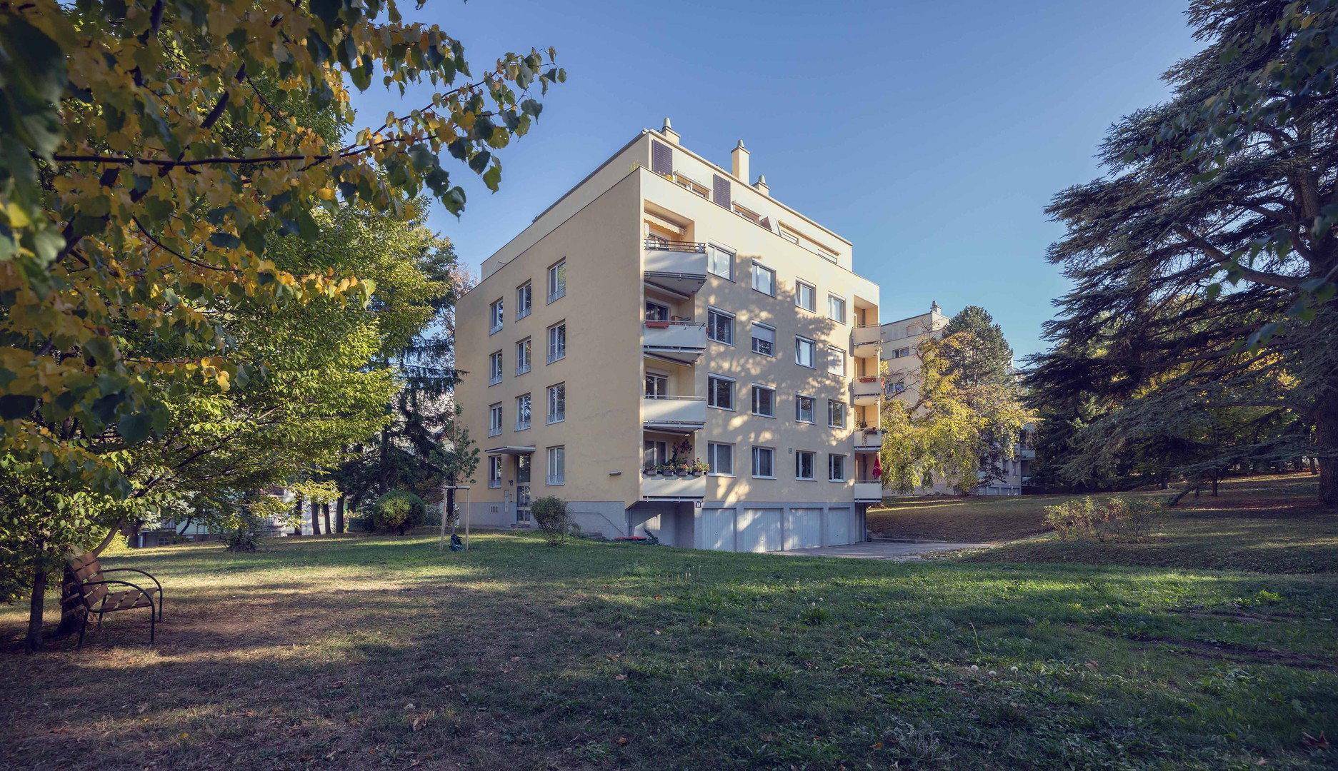 Modernes Wohngebäude mit mehreren Etagen, Balkonen und umgebender Grünfläche.