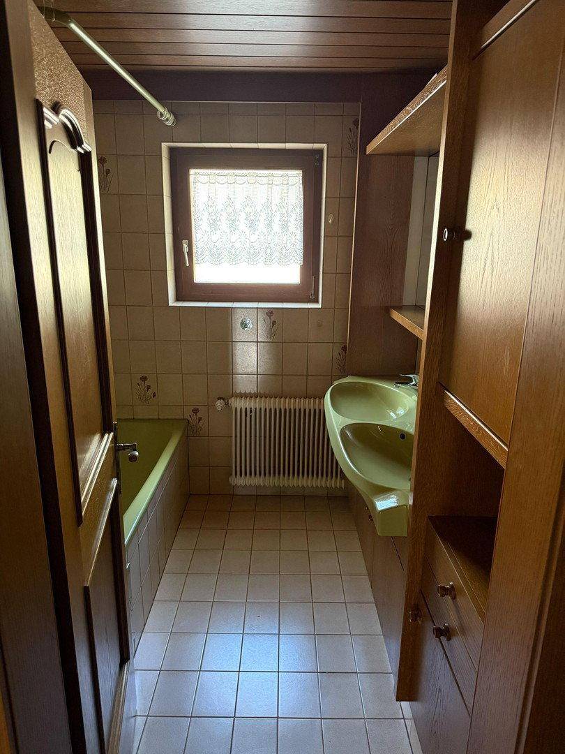 Badezimmer im Stil der 80er Jahre mit grüner Badewanne, Waschbecken und Fliesen.