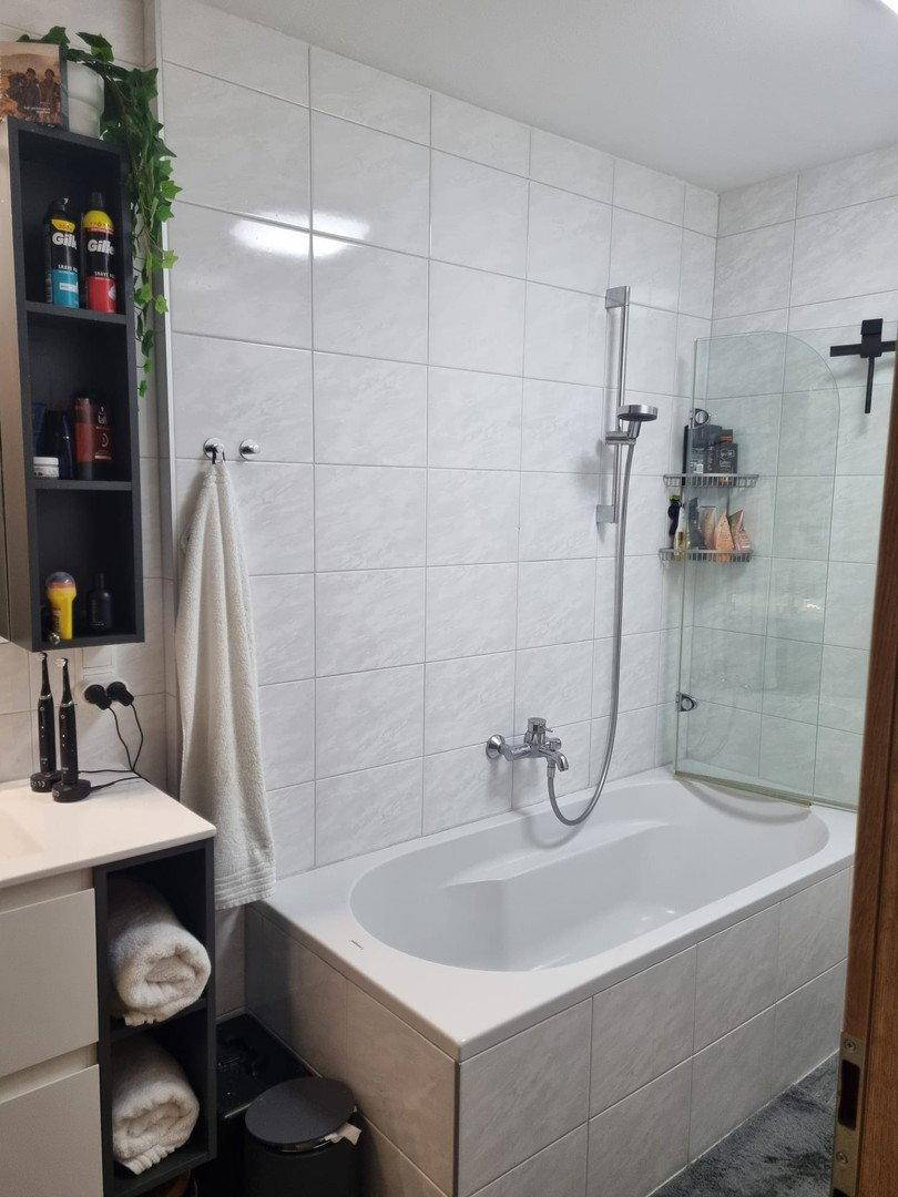 Modernes Badezimmer mit Badewanne, Duschabtrennung und hellen Fliesen an den Wänden.